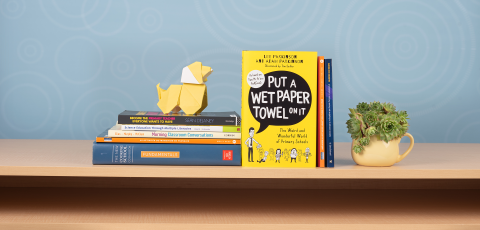 Books displayed on a shelf in front of a blue background with an origami dog and coffee cup with a succulent plant.