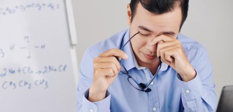 Middle age man rubbing holding his glasses and rubbing his eyes infront of a white board with equations