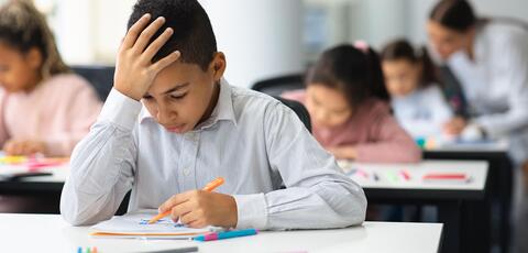 Boy at desk with head in hand as he looks down at classwork