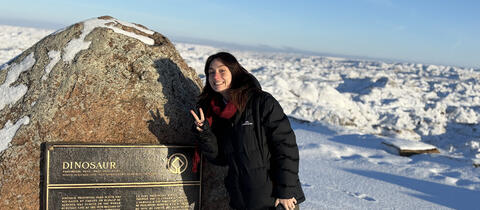 A woman stands beside a plaque on top of a mountain