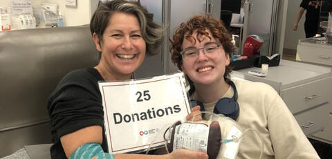 Teacher with a student at a blood donation center holding a 25 donations sign