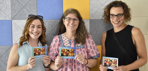Three women holding event postcard