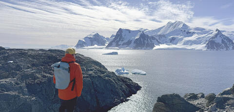 A man stands on a rocky shore looking at out icebergs 