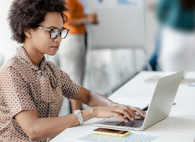 A Black woman with an afro sits at a desk in front of her laptop