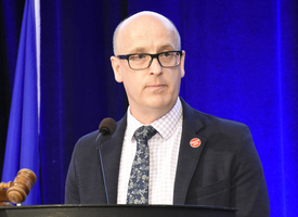 ATA president Jason Schilling stands on stage behind a podium in a suite and tie