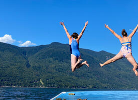 Two women jumping into an Okanagan lake under a blue sky