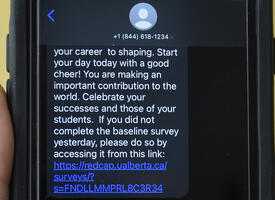 Hand holding an iPhone with the text app open and messages from Wellness4Teachers