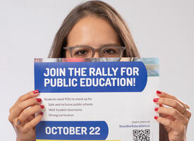 Women with red nails holds a poster for a public education rally on October 22