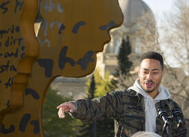 Rapper Cadence Weapon standing in front of the 100th Anniversary sculpture at the Alberta Legislature 
