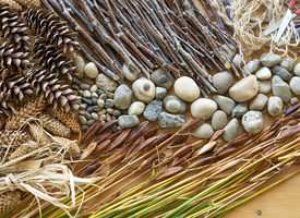 A collection of pine cones, twigs, stones, willow and straw seen from above, on a wooden table