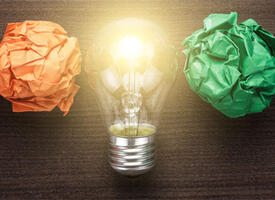 Paper in a rainbow of colours crunched into balls in a line, in the middle an illuminated light bulb