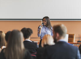 Young women of colour speaking to an audience in front of a white board