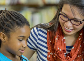 A teacher sits with a student at a desk
