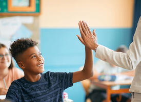 A young black student giving a high five to a teacher
