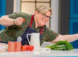 Contestant in a tv cooking show reaches across a counter with an apron on