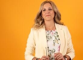 Krimsen Sumners wearing a beige blazer in front of orange background