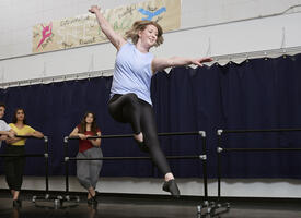 Dancer leaping in a studio with three student watching