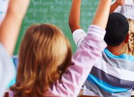 Back of students in classroom all raising their hands