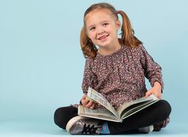 Young girl with pigtails sitting cross-legged with a book 