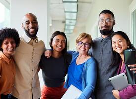 Diverse smiling adults standing with arms around each other in a hallway