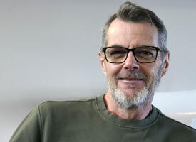 Man in 60's wearing a green sweater, beard and glasses