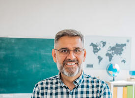 A gray-haired man with a beard and glasses in a green and white ch