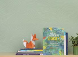 A green wall with 8 books in front of it. A plant in a coffee cup stands on one side and an origami fox on the other side.