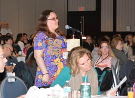 Women standing at mic in the middle of a conference room