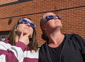 Two women look at the solar eclipse through protective glasses