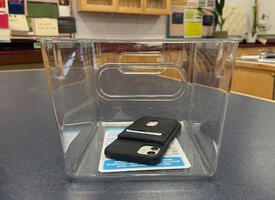 Cellphone sitting in transparent bin on desktop