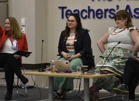 Four women sit on a panel at the front of a conference presentation