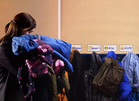 A teacher holds an armful of coats outside her classroom