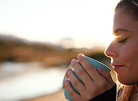 A women sips coffee next to a river