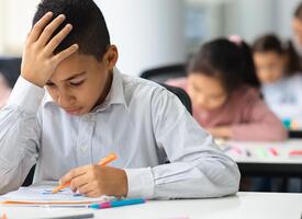 Boy at desk with head in hand as he looks down at classwork