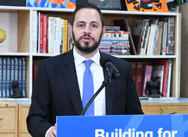Man wearing blue tie speaks and a podium with sign reading Building for the Future
