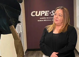 women in black blazer holding a sheet of paper infront of the CUPE logo