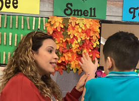Teacher guides a student's hand over a sensory wall