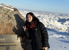 A woman stands beside a plaque on top of a mountain