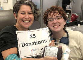 Teacher with a student at a blood donation center holding a 25 donations sign
