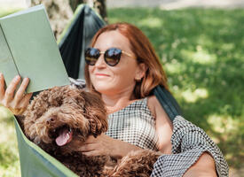 Women laying in a hammock reading a book with her doodle dog