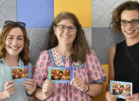 Three women holding event postcard
