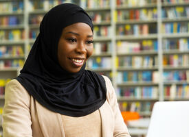 A woman in a hijab using a laptop in a library. 
