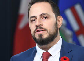 Education Minister infront of flags wearing a poppy in a blue suit