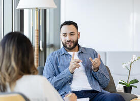 Young man with beard wearing a denim shirt talks with a women in a white shirt