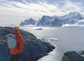 A man stands on a rocky shore looking at out icebergs 