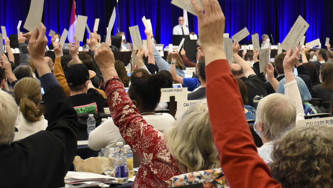 Attendees at annual assembly vote with arms raised and tickets in hand.