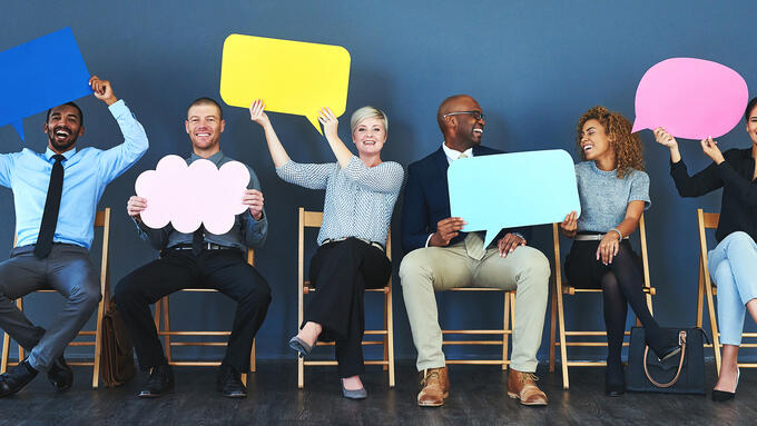 Group of adults sitting on chairs holding blank speech bubbles made of coloured paper
