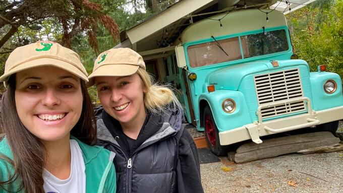 Two women pose in front of blue schoolbus