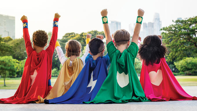 5 children faced away from the camera wearing different coloured superhero capes with hearts, lightning bolts and shields on the back.