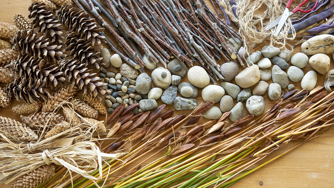 A collection of pine cones, twigs, stones, willow and straw seen from above, on a wooden table
